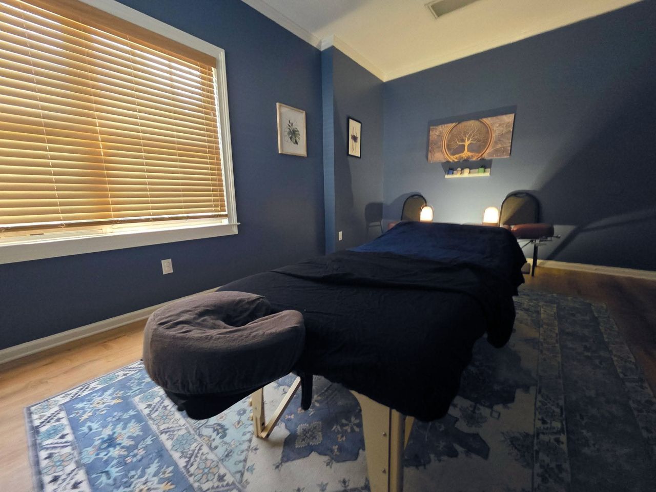 The Elbow Room treatment room at Stauffer Chiropractic: a massage table with a covered face cradle, two lanterns glowing at the far wall, and daylight through wood blinds