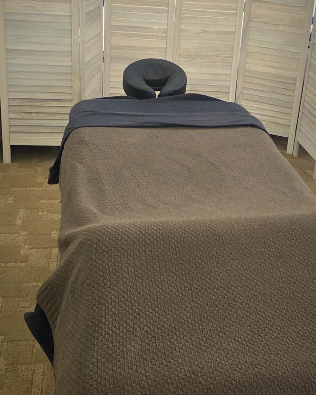 The massage room at the Cherokee Center for Change: a massage table in dark linens and a gray knit throw, with a face cradle, in front of a white louvered screen